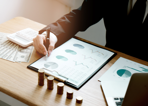 Eine Klemmbrett mit einem Zettel auf einem Tisch, welcher von jemandem beschrieben wird. Daneben Geldscheine und Münzen.