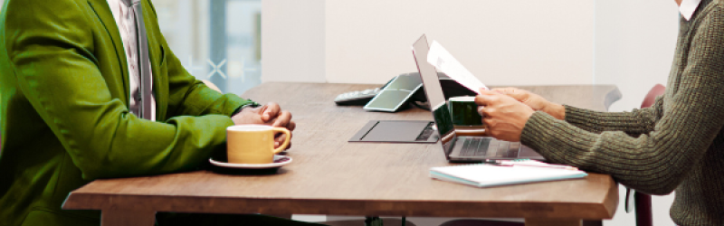 Zwei Personen in Business-Kleidung an einem Schreibtisch, offensichtlich am Arbeiten.