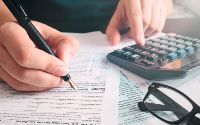 Jemand füllt einen Antrag an einem Tisch mit einem  und Taschenrechner aus