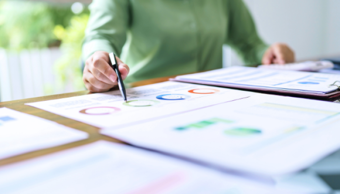 Hände, die mit einem Kugelschreiber auf einem Tisch auf Grafiken auf einem Zettel zeigen.